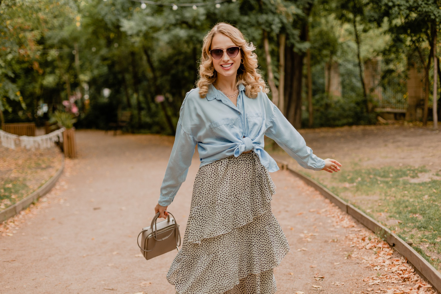 Fotografia de moda feminina mostrando uma mulher usando saia estampada fluida com camisa azul clara em cenário de outono, referência de look elegante para a estação.
