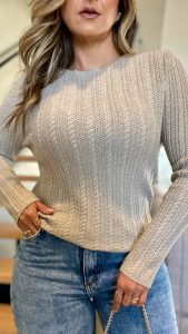 Modelo usando blusa de tricot bege de manga longa com textura trançada em relevo, combinada com calça jeans clara.