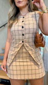 Mulher usando conjunto xadrez bege com bolsa caramelo e sandália preta, em escada moderna