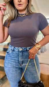 Modelo usando t-shirt básica gola alta cinza chumbo de manga curta com calça jeans clara e acessórios dourados.